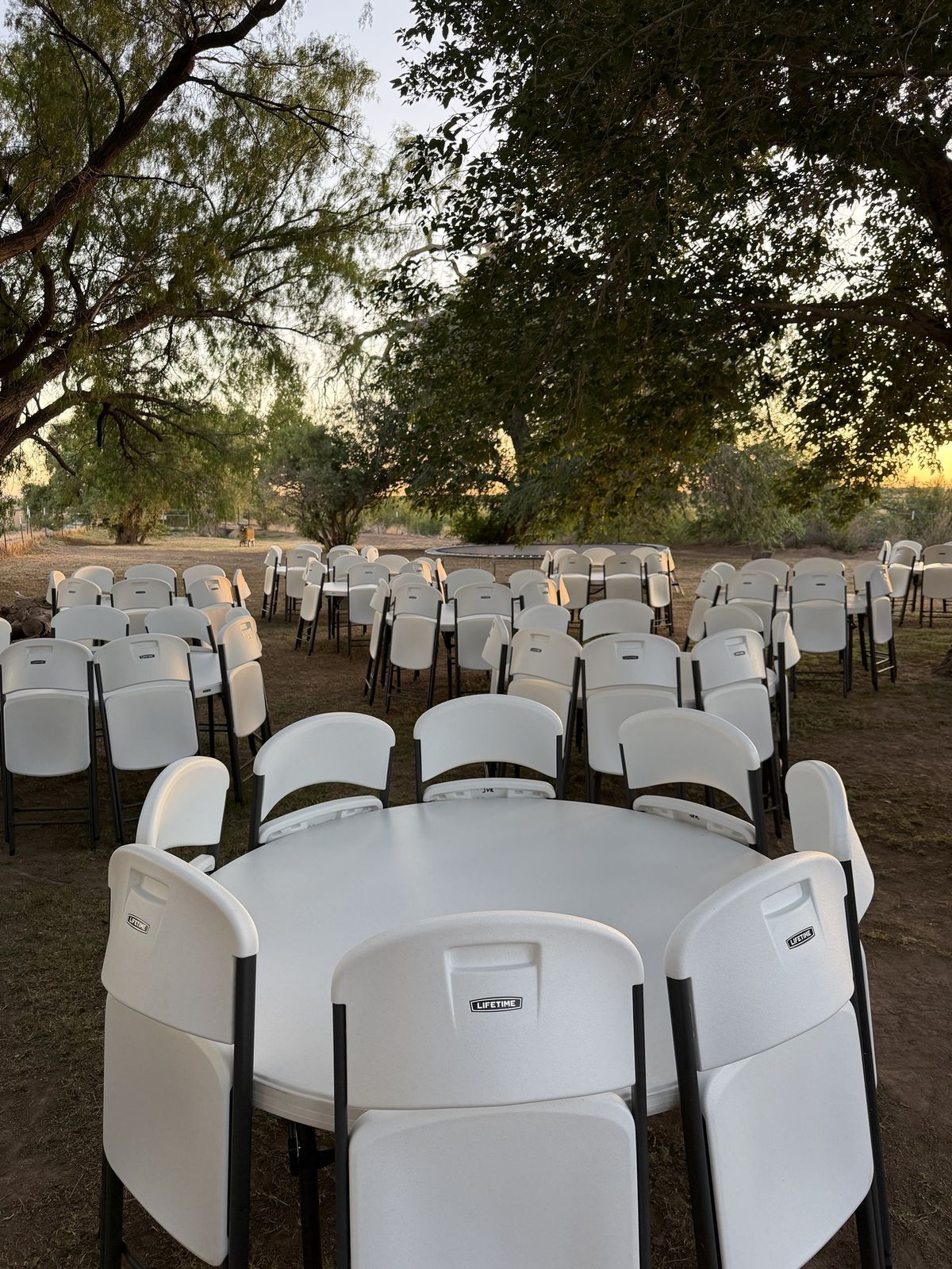 Large outdoor event with round tables and Lifetime chairs under trees in El Paso