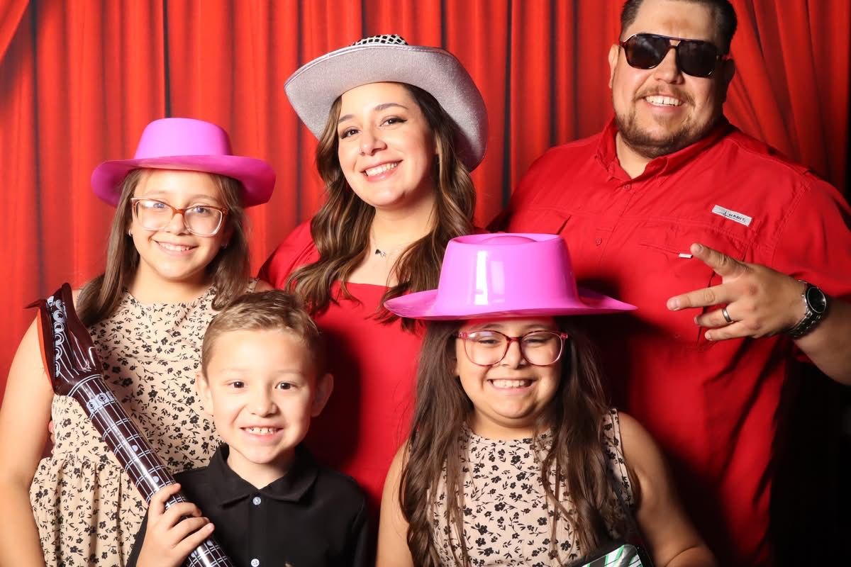 Family with hats and props at the JVR photo booth with red curtain backdrop
